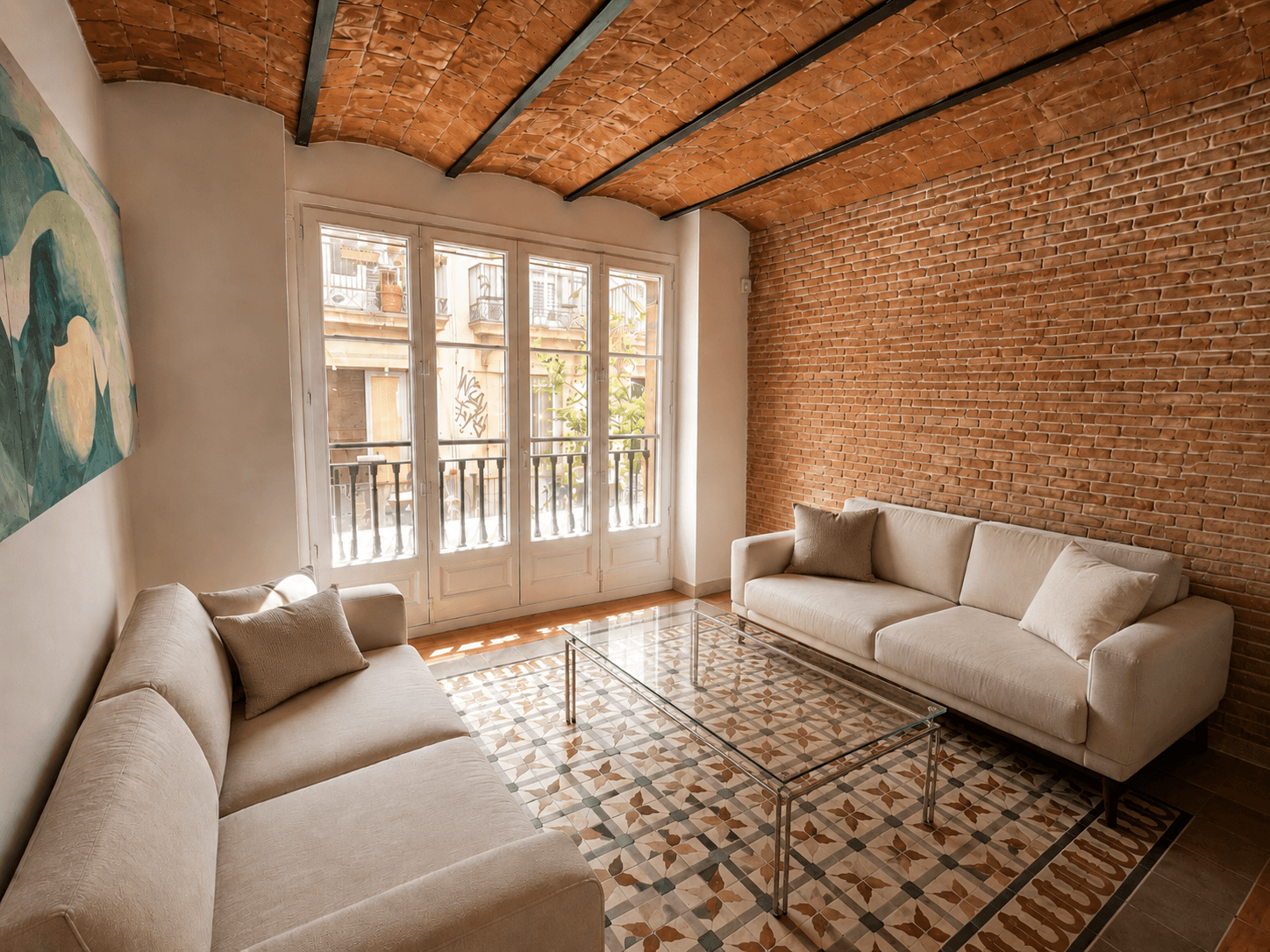 Salón con bóveda de ladrillo, dos sofás claros, mesa baja de cristal y suelo de mosaico hidráulico frente al balcón.